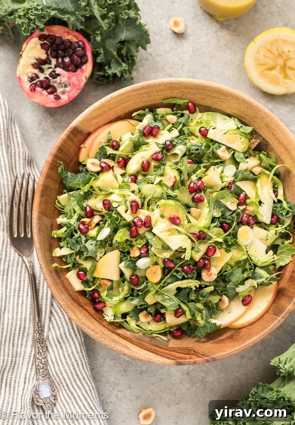 A vibrant Kale and Brussels Sprout Salad in a teak bowl, garnished with fresh pomegranates.