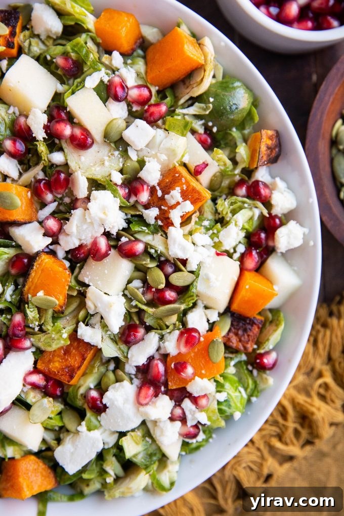 A healthy Shaved Brussel Sprout Salad with Roasted Butternut Squash, apple, pomegranate seeds, feta cheese, and pumpkin seeds.