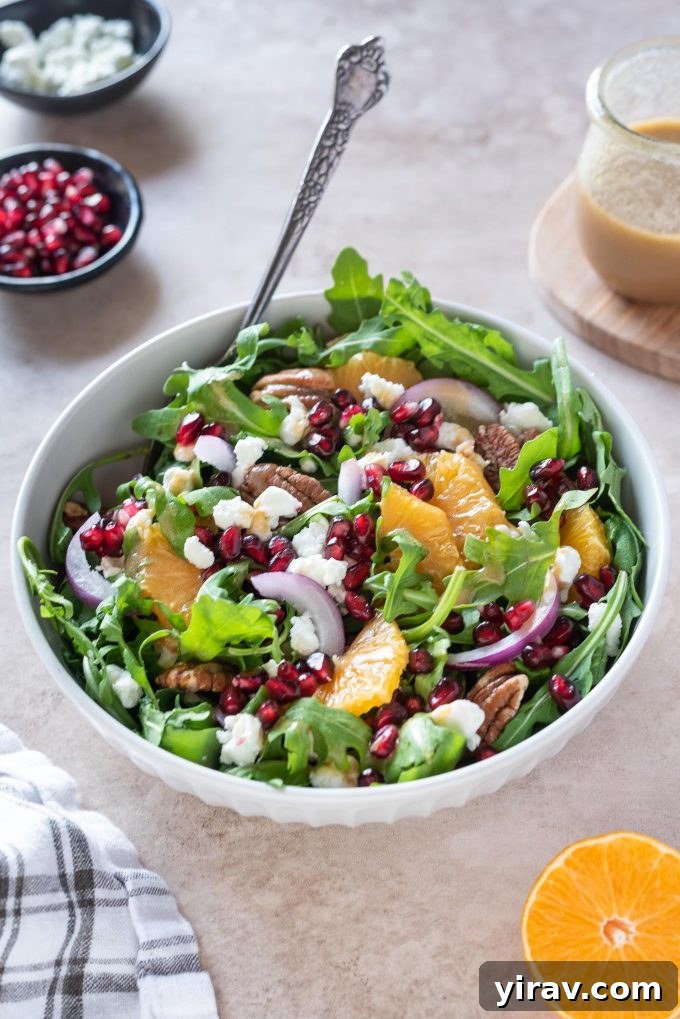 Arugula orange pomegranate salad served in a white bowl, with a fork digging in to reveal the fresh ingredients.