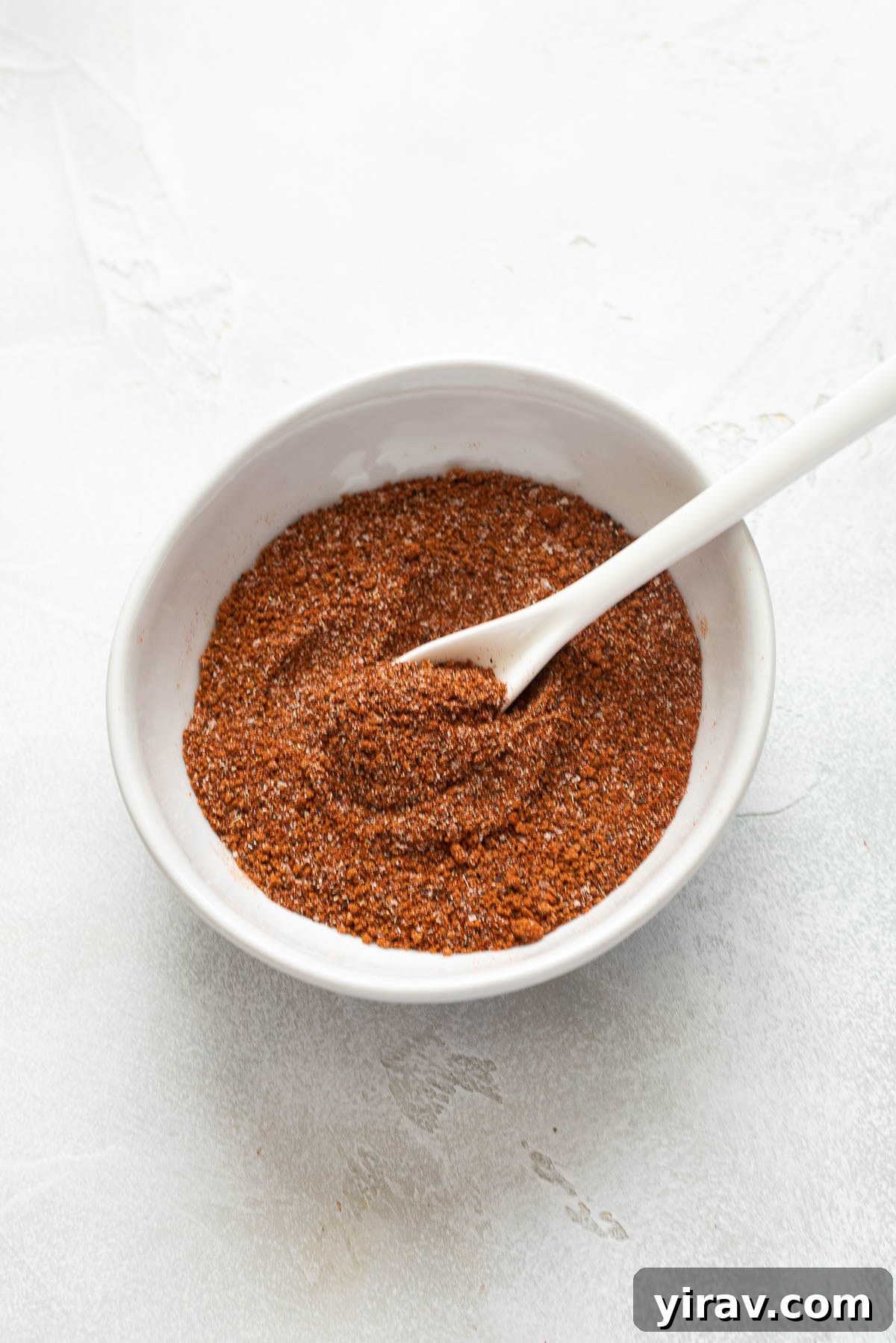 Smoky Sweet Chicken Coating 2 A bowl filled with homemade BBQ chicken rub, with a spoon resting in the middle, ready to be used on grilled meats.