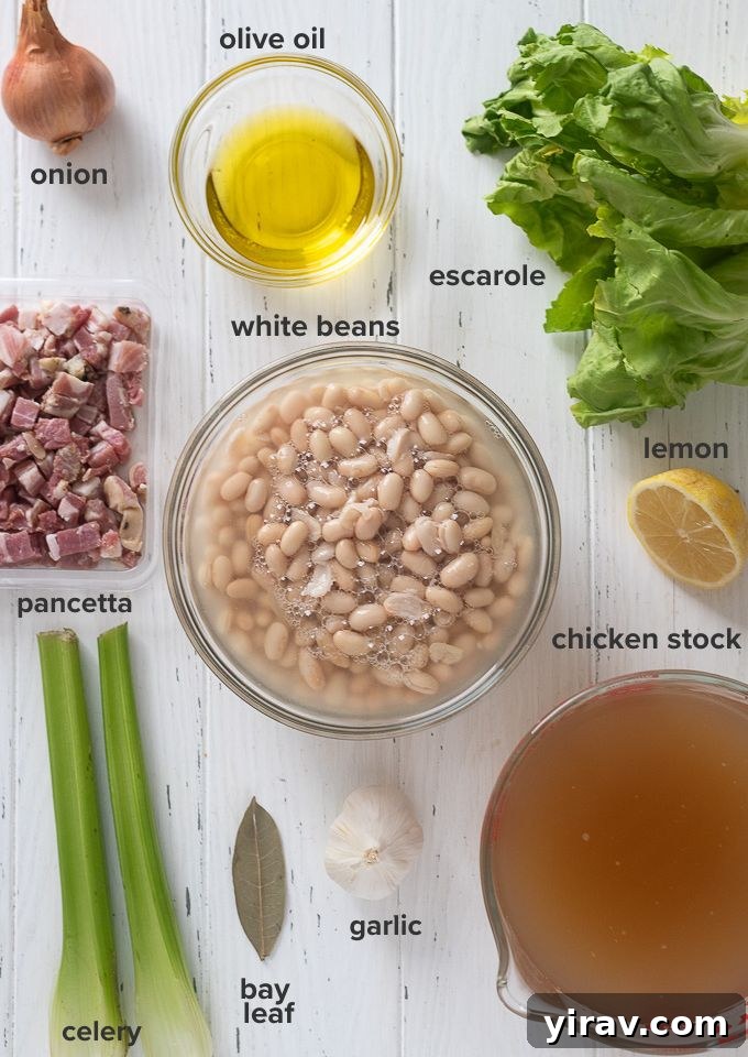 A flat lay photograph showcasing all the fresh ingredients needed for Escarole and Bean Soup, including escarole, white beans, pancetta, and aromatics.