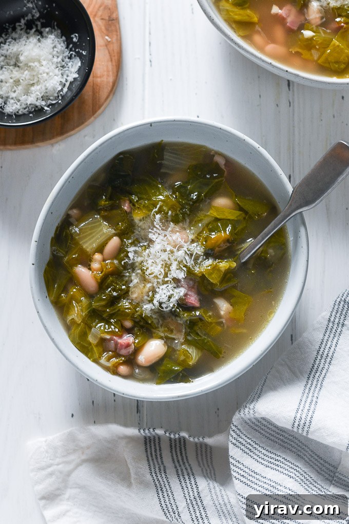 A close-up of a bowl of Escarole Soup, topped with a generous amount of freshly grated Parmesan cheese and a drizzle of olive oil.