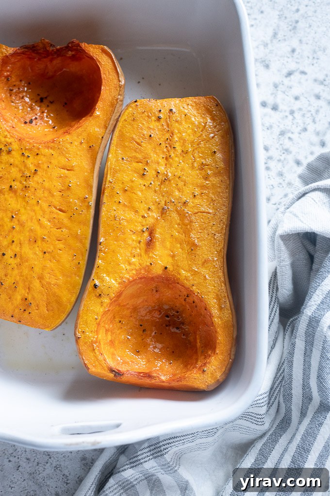 Two halves of roasted butternut squash in a ceramic baking dish, ready to be scooped.