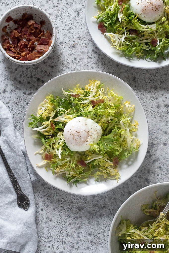 Two plates of Salade Lyonnaise with generous servings of frisée, crispy bacon, and a perfectly poached egg on top.