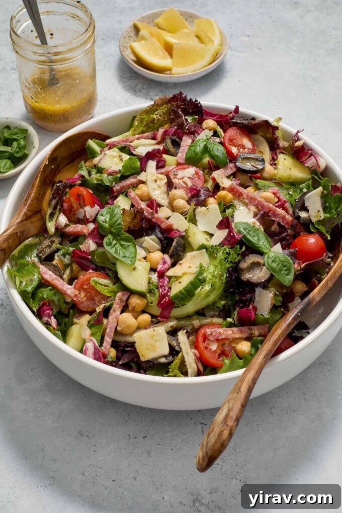 Italian chopped salad in a bowl with a jar of dressing and basil garnish