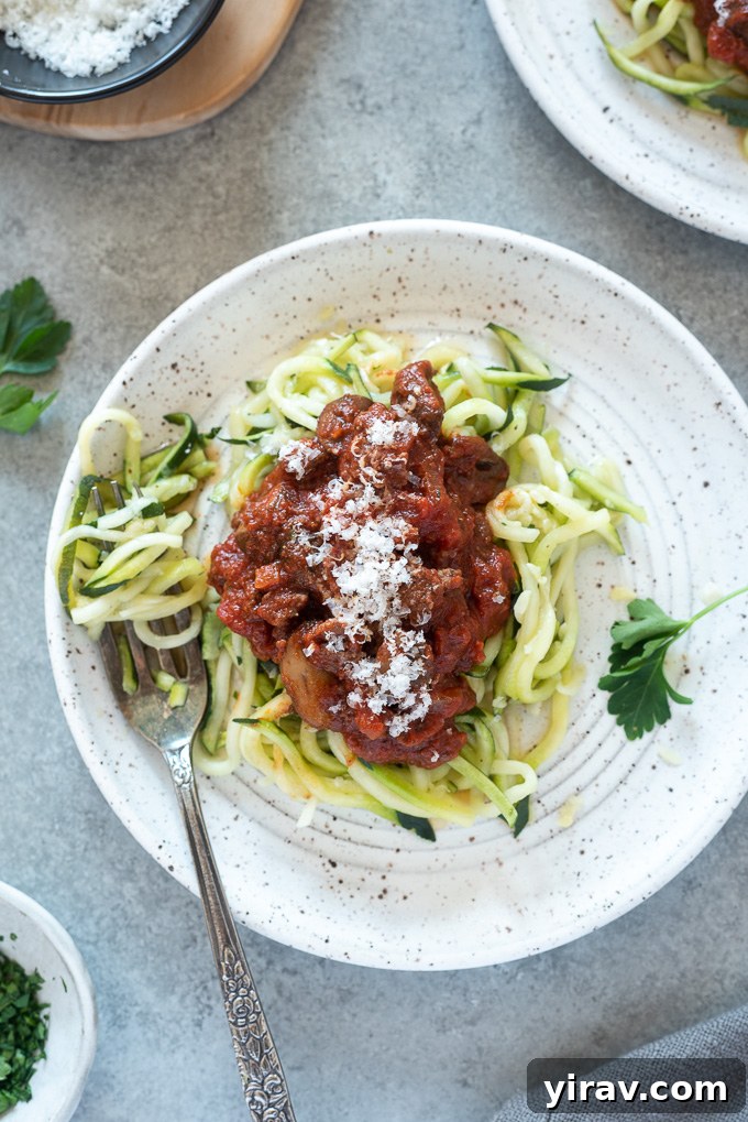 Homemade meat sauce generously spooned over a bed of fresh zucchini noodles on a white plate.