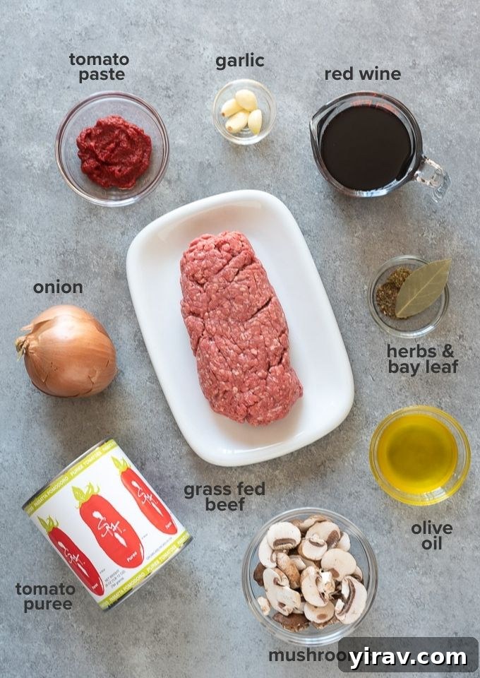 Various ingredients for homemade meat sauce, including ground beef, mushrooms, tomatoes, and herbs, arranged on a rustic wooden board.