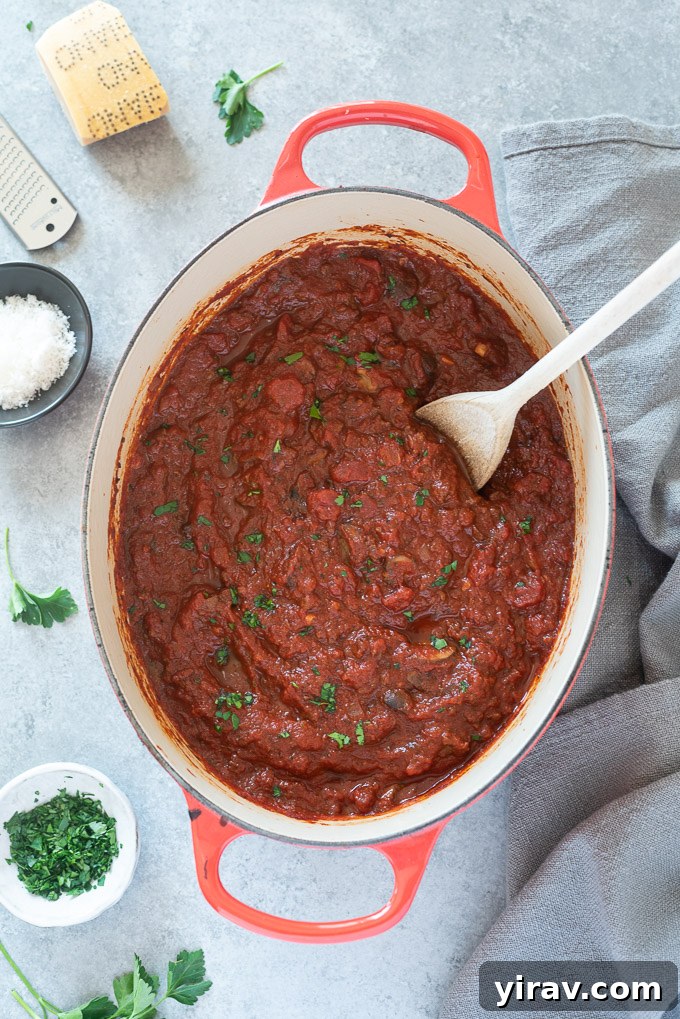Rich homemade meat sauce in a rustic Dutch oven with a wooden spoon resting inside.