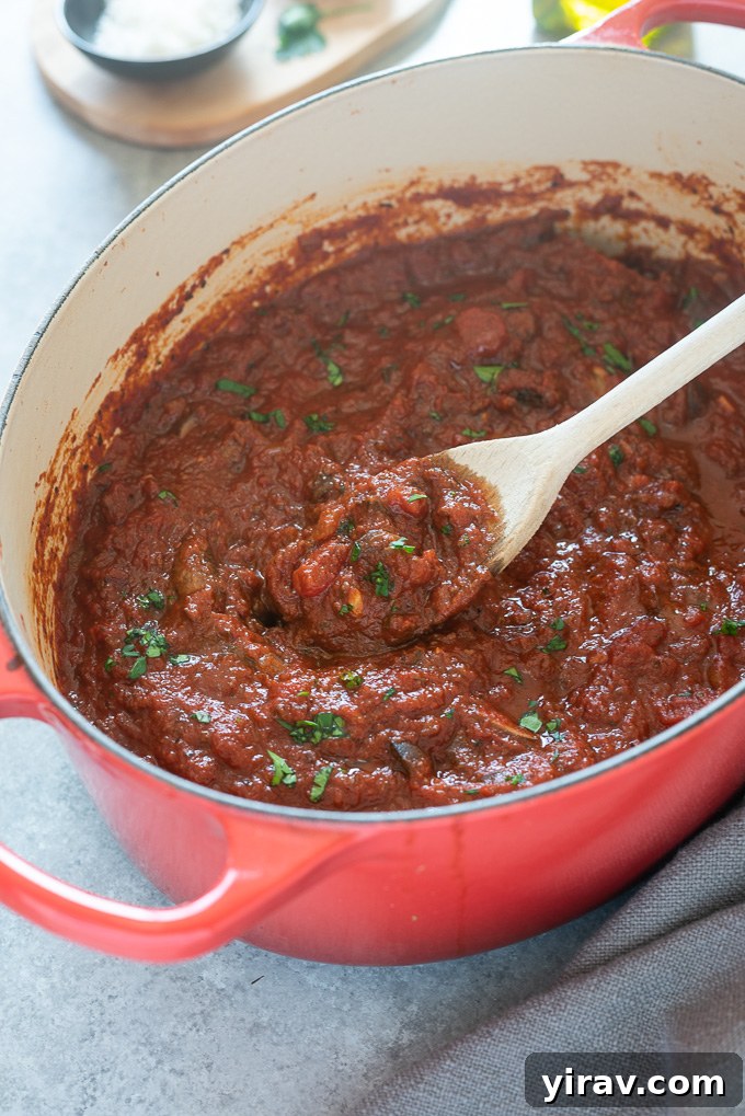 A wooden spoon lifted from a Dutch oven, full of rich homemade meat sauce.
