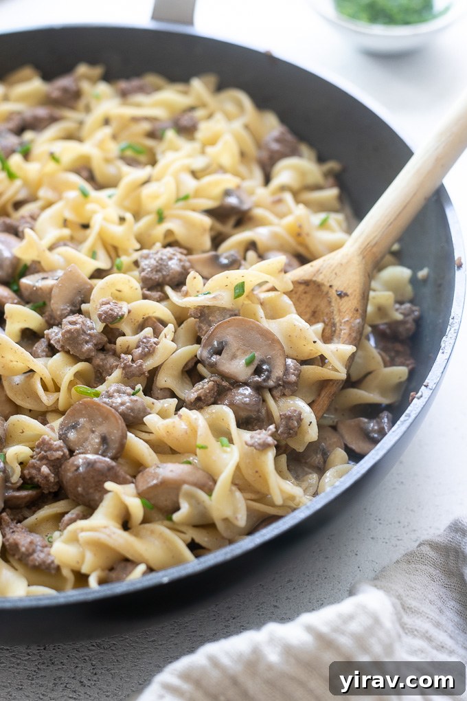 A wooden spoon stirring into a skillet of one pot hamburger stroganoff, highlighting the creamy texture.
