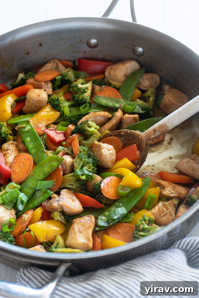 Chicken veggie stir fry in a skillet with wooden spoon digging in