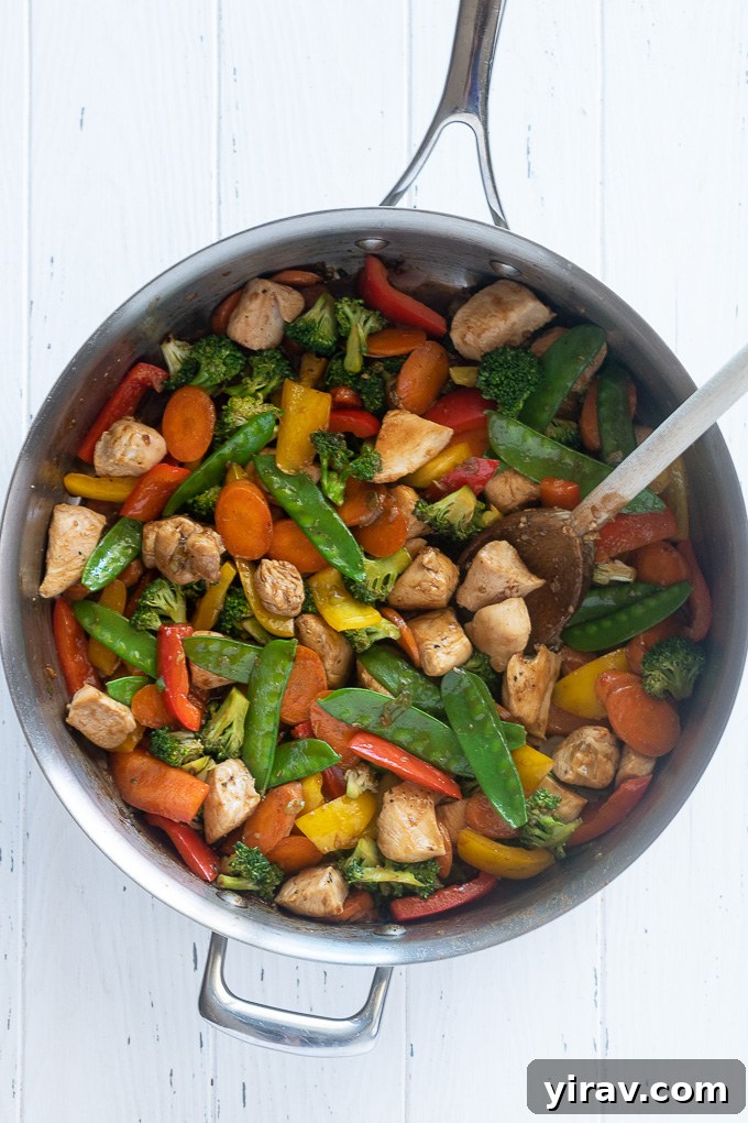 Chicken and vegetable stir fry in a skillet with wooden spoon