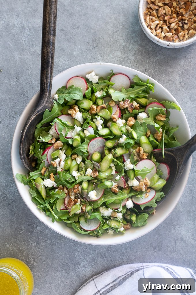 Raw asparagus salad tossed with arugula and goat cheese in a white serving bowl