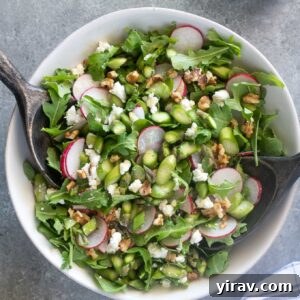 Asparagus salad in a white bowl with salad servers digging in