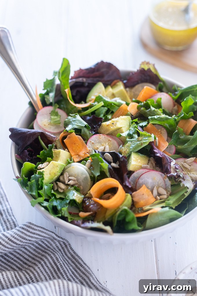 A large bowl of fresh spring mix salad, showing crisp green leaves, with salad servers poised to serve, emphasizing healthy eating.