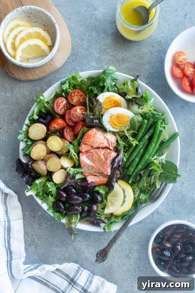 Gourmet Salmon Nicoise Salad with wild salmon, crisp greens, vegetables, hard-boiled egg, potatoes, and olives, with ingredients surrounding.