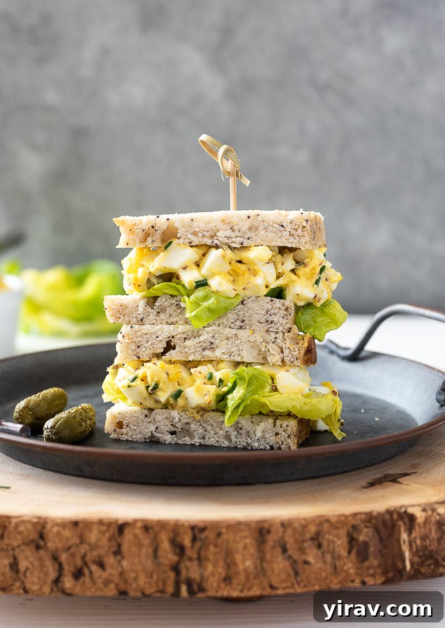 Two generous egg salad sandwiches piled high on a plate with a wooden pick, highlighting a creamy and flavorful filling.