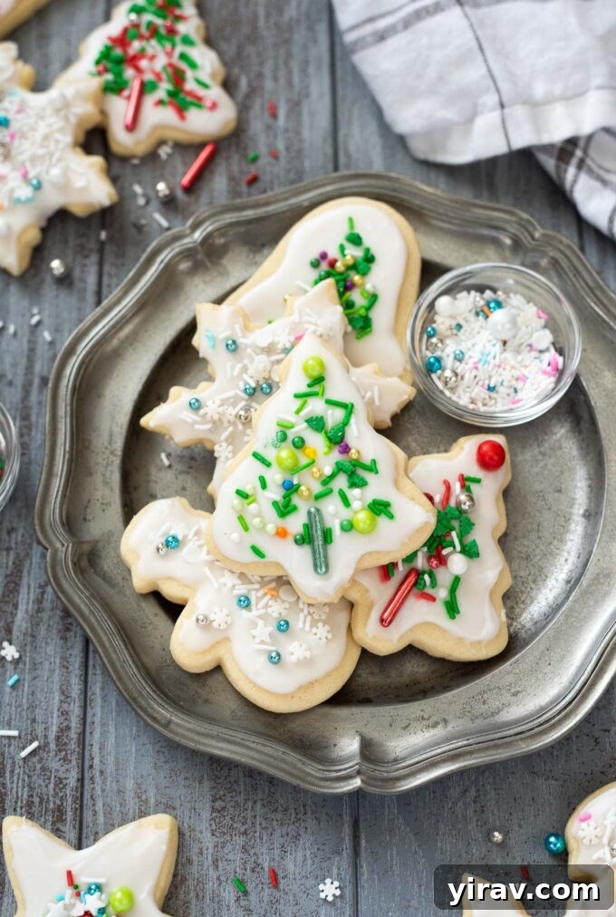 Beautifully decorated Christmas sugar cookies on a white plate with colorful sprinkles scattered around.
