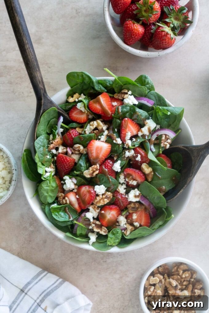 Strawberry spinach salad in a bowl with salad servers, ready to be served.