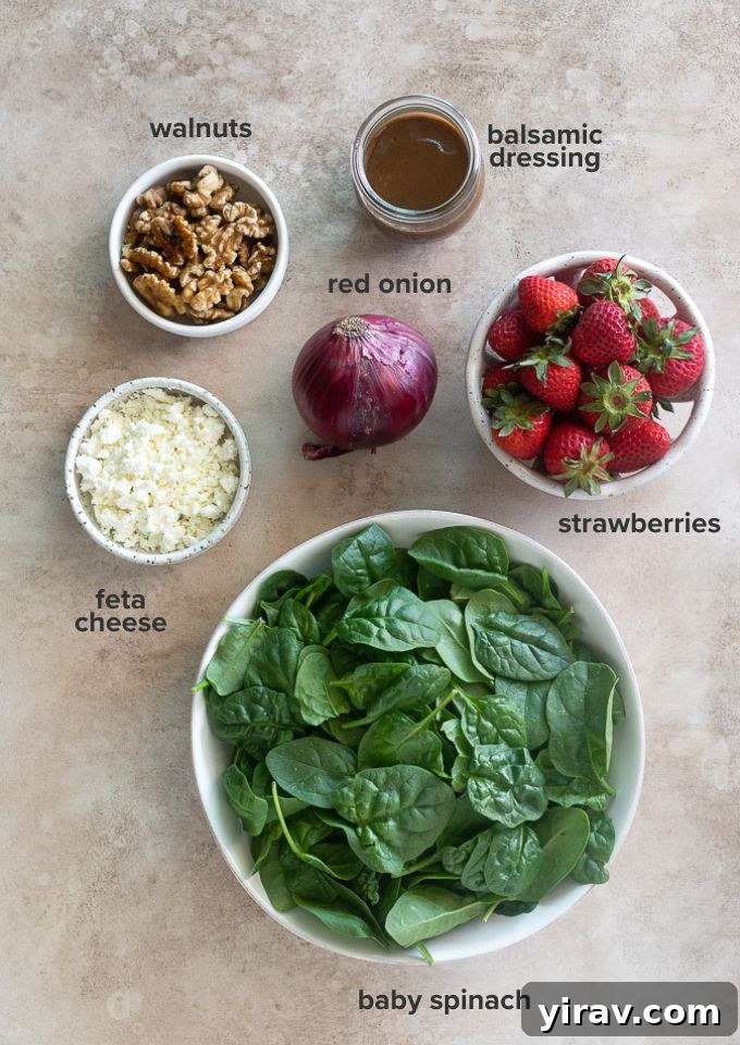 A selection of fresh ingredients including strawberries, spinach, red onion, feta, and walnuts for the salad recipe.