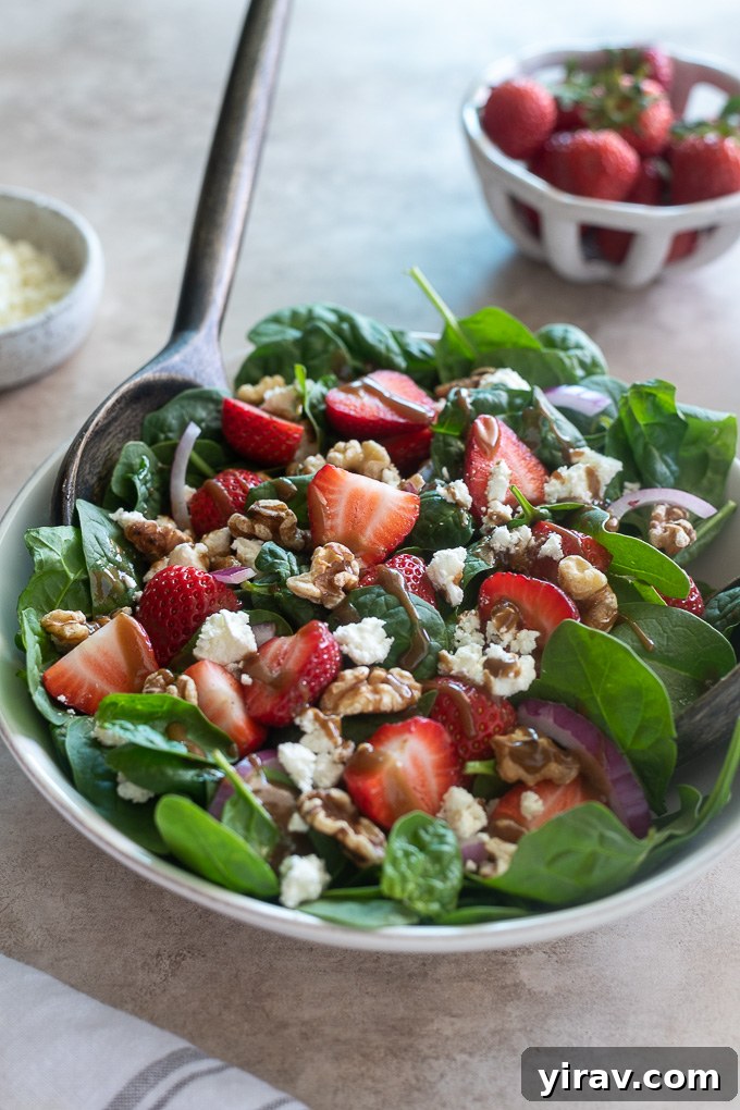 A serving of spinach and strawberry salad in a white bowl with a serving spoon.