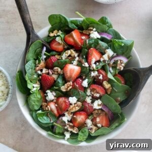 Strawberry spinach salad in a bowl with salad servers, a smaller image for the recipe card.