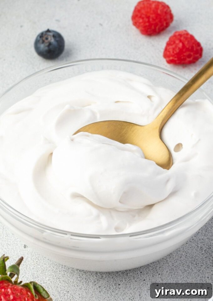 A spoonful of fluffy coconut whipped cream in a clear glass bowl, showcasing its light and airy texture. Ideal for dairy-free and vegan diets.