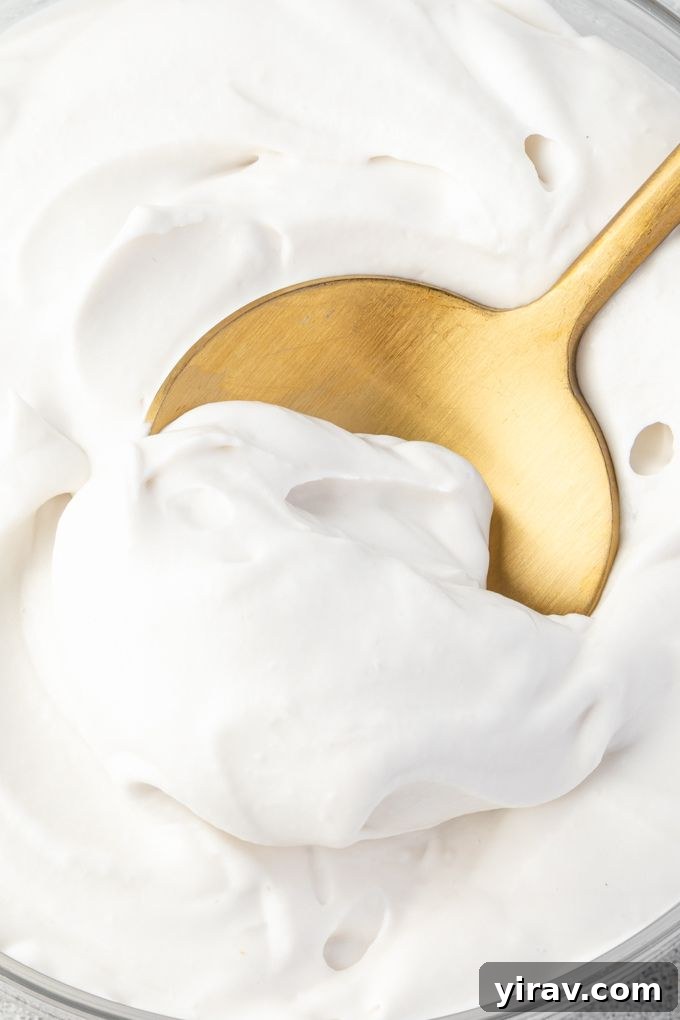 A close-up shot of coconut whipped cream in a serving bowl, with a spoon gently scooping into its light and airy texture.