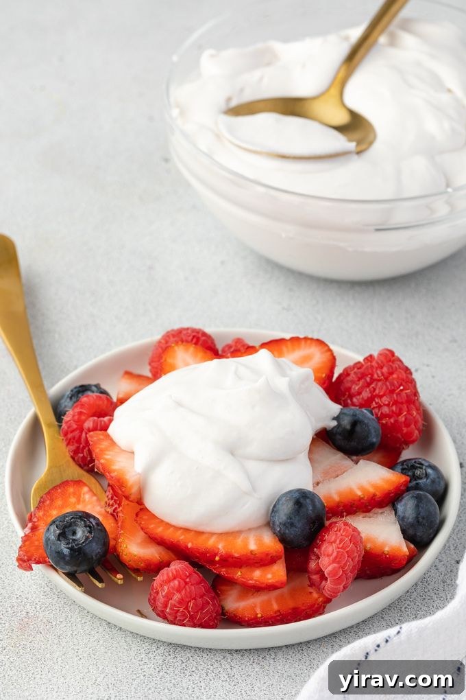 A delectable dessert featuring a generous dollop of coconut cream whipped cream artfully placed over a vibrant medley of fresh berries, ready to be enjoyed.