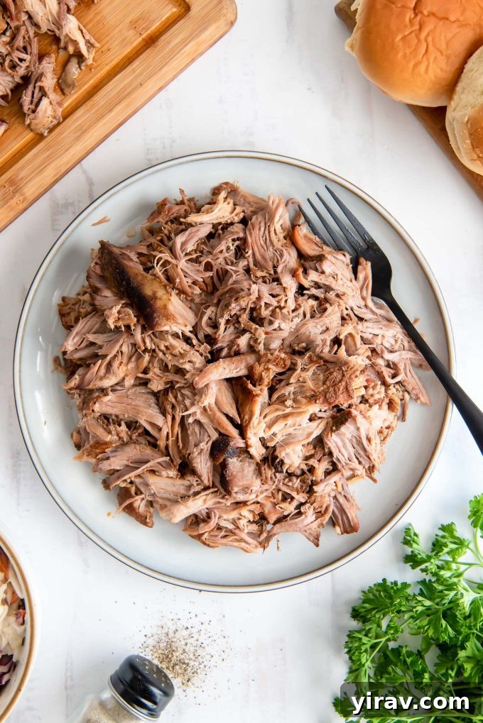 Slow cooker pulled pork on a white plate, garnished with fresh herbs