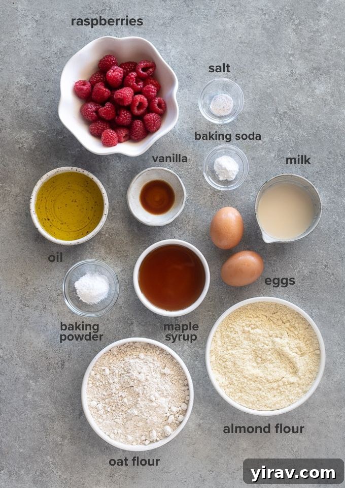 A vibrant flat lay of all the essential ingredients needed for healthy raspberry muffins, including fresh raspberries, flours, eggs, and liquids.