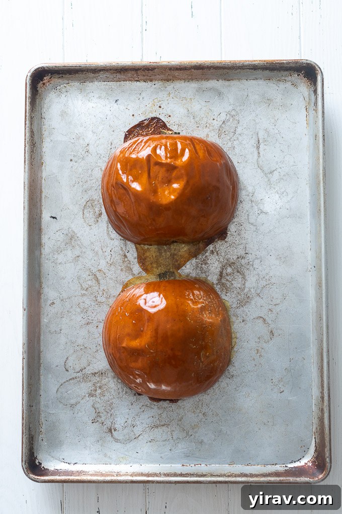 Two roasted pumpkin halves, cut side down, perfectly caramelized on a baking sheet.