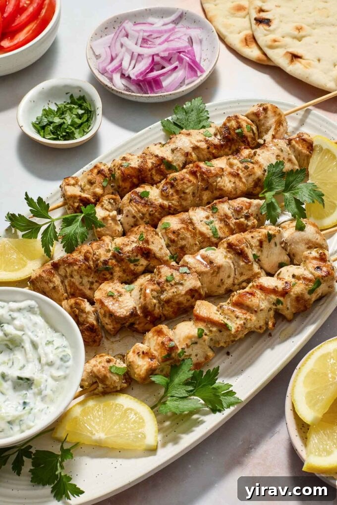 Easy Greek Chicken Souvlaki on a platter with lemon slices, fresh oregano, and a bowl of tzatziki.