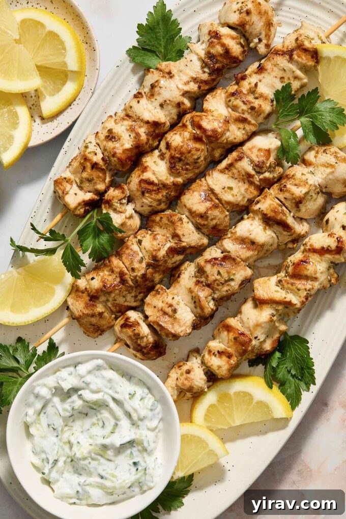 Grilled chicken souvlaki on skewers with a side of tzatziki and lemon wedges.