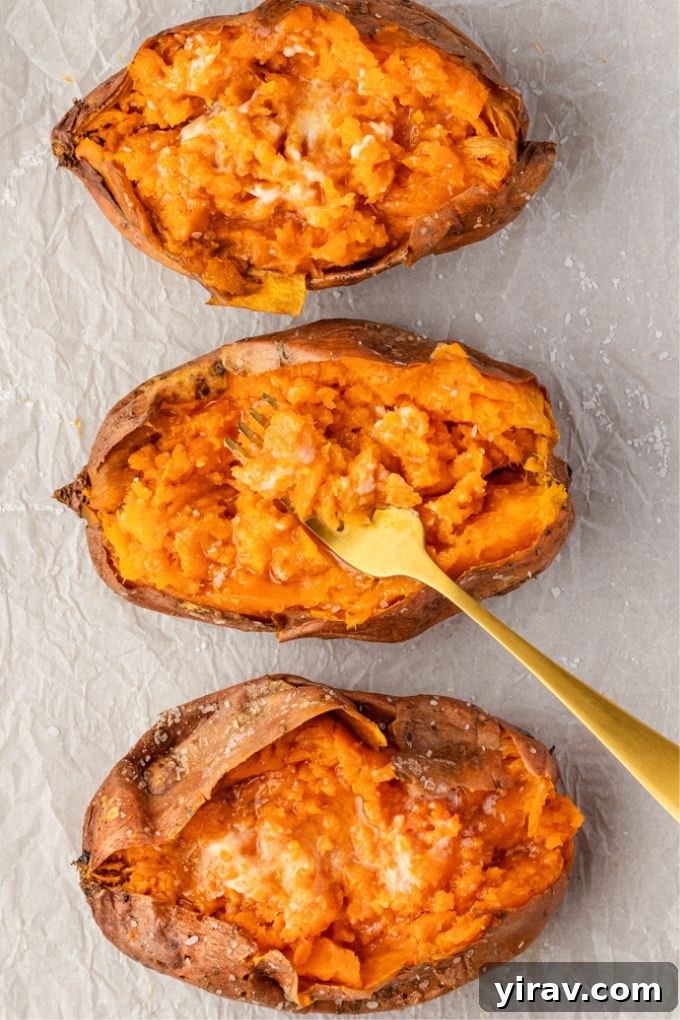 Baked sweet potatoes with a fork digging into the middle one, showing a fluffy interior