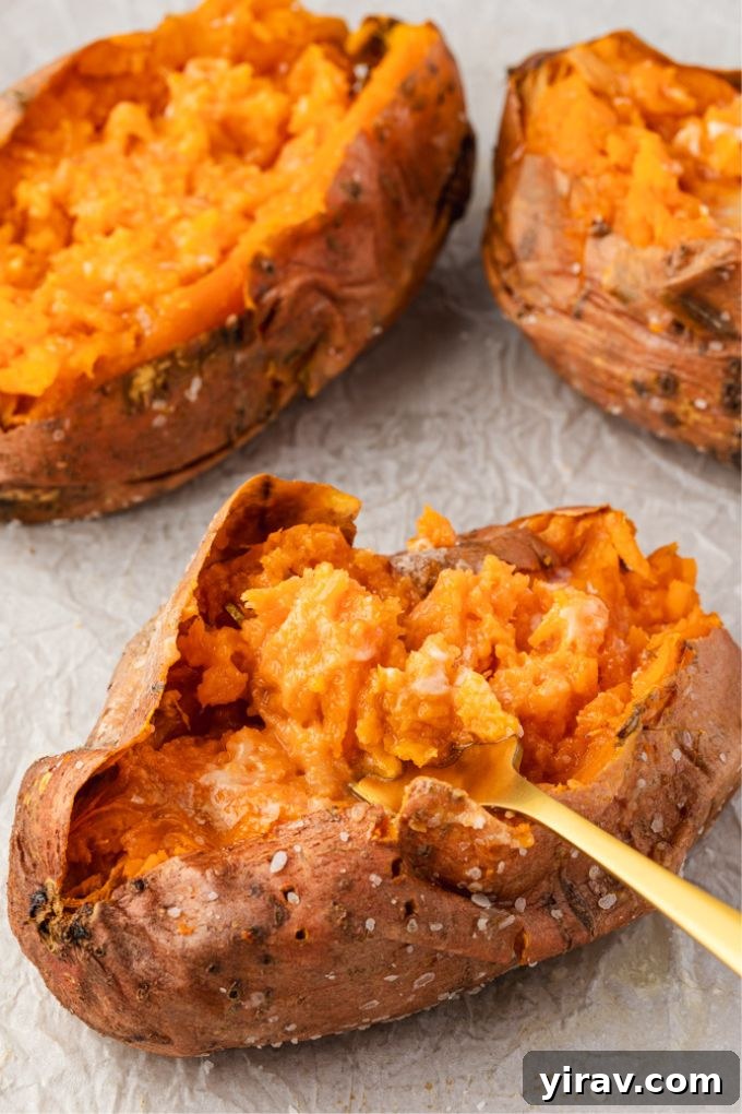Oven baked sweet potatoes with a fork fluffing one up, showing the soft interior