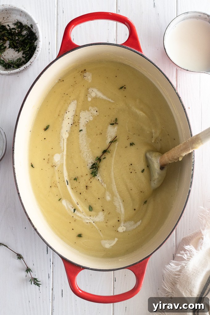 Parsnip soup in a dutch oven with a thyme sprig and wooden spoon