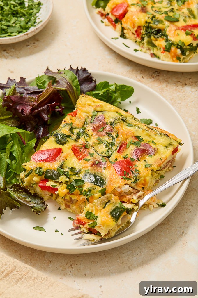 Effortless Bacon and Egg Bake 7 Close-up of a serving of Bacon and Egg Casserole on a plate, with a fork digging into the fluffy eggs and visible pieces of bacon and vegetables.