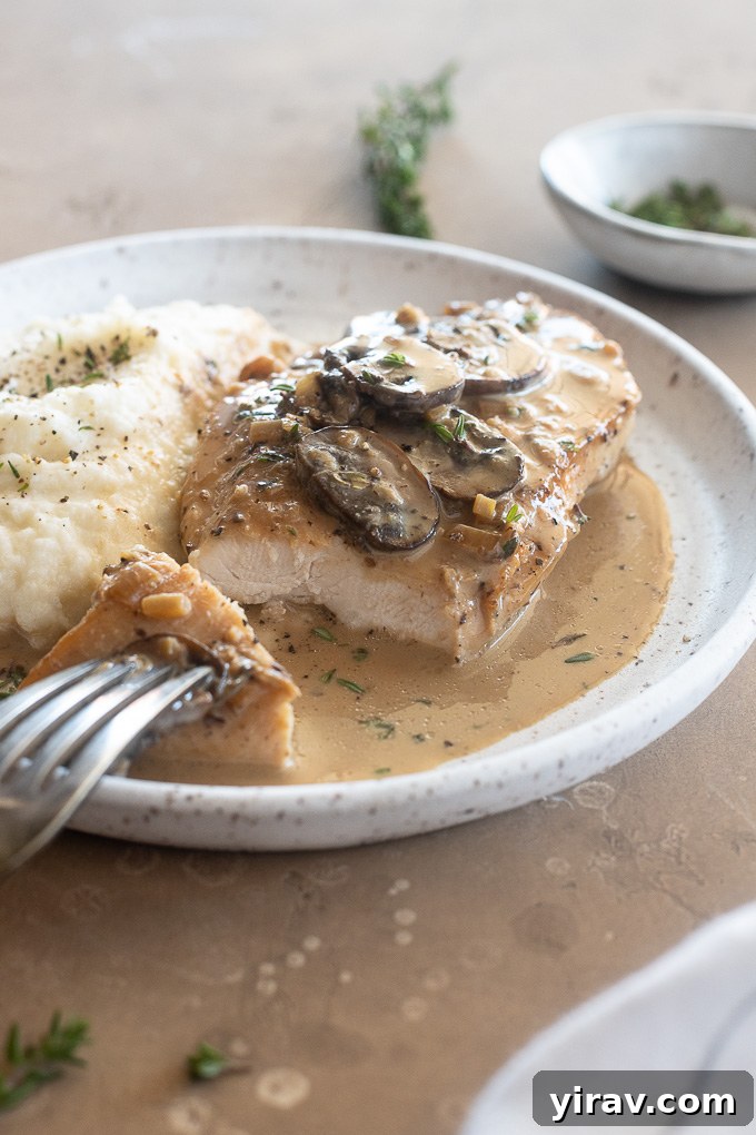 A serving of Creamy Marsala Chicken with a piece removed, showing its tender interior, on a white plate with a fork.