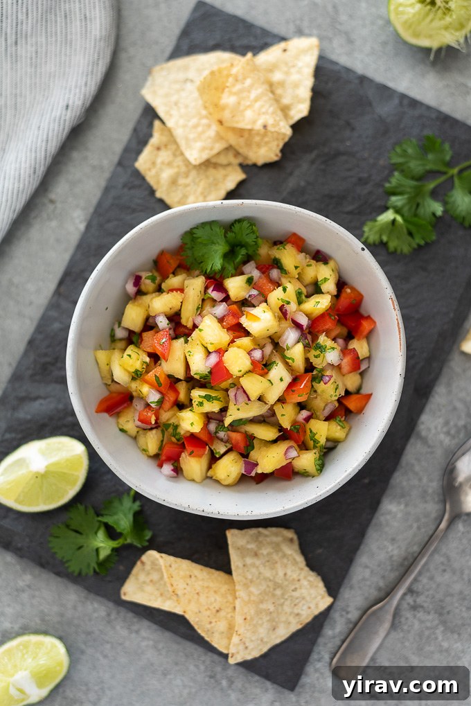 A beautifully arranged platter featuring a bowl of pineapple salsa, surrounded by crunchy tortilla chips, fresh lime wedges, and cilantro sprigs.
