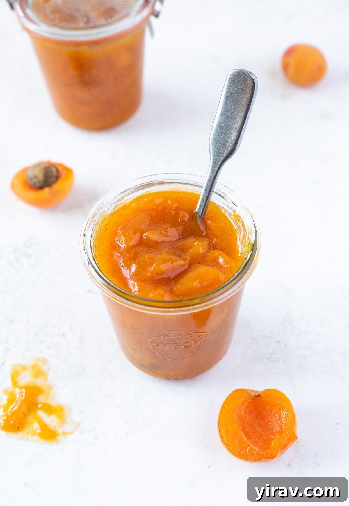 Handcrafted Golden Apricot Jam 2 A jar of homemade small batch apricot jam with a spoon buried into its center, showcasing its thick, golden texture.