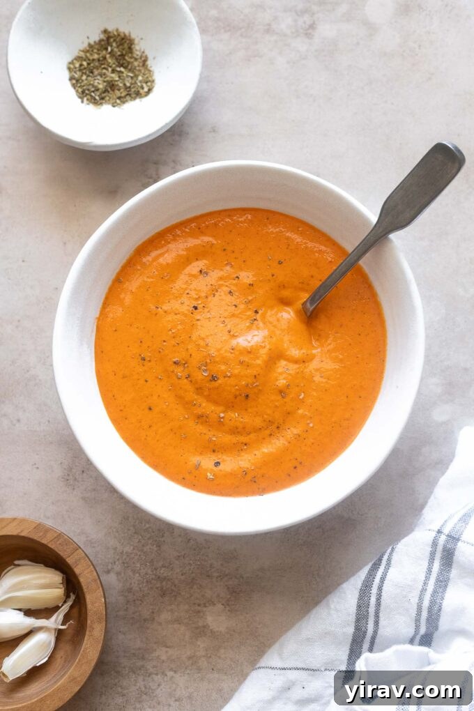 Creamy roasted red pepper sauce in a bowl with a spoon, garnished with fresh herbs.