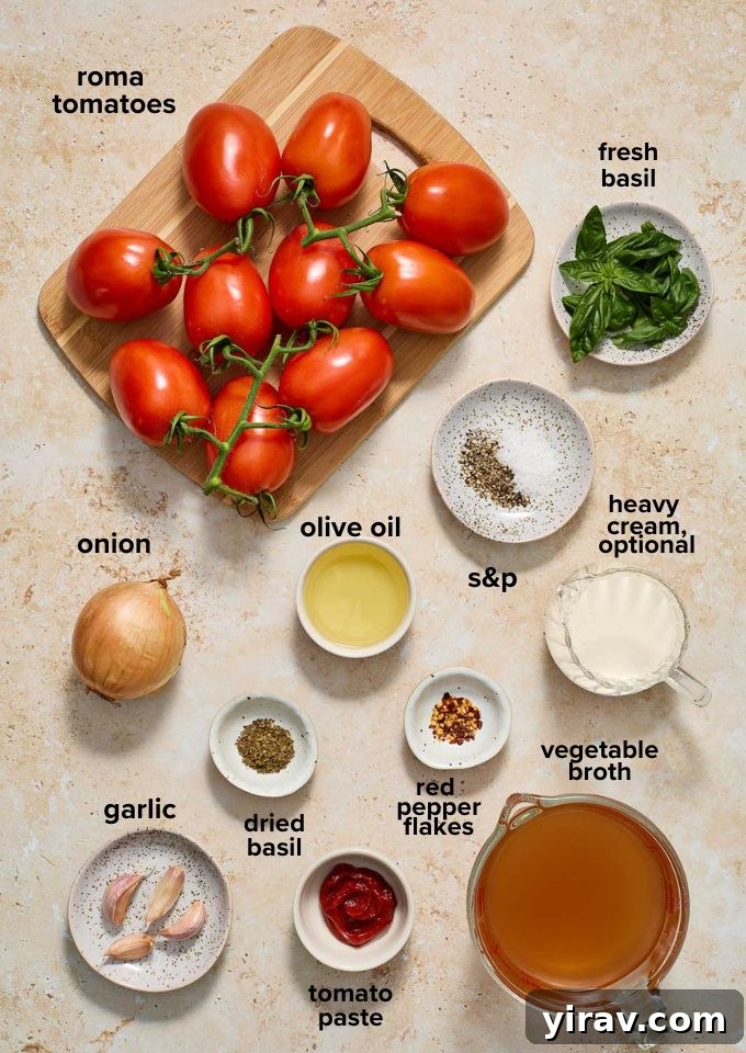 Arrangement of fresh roasted tomato soup recipe ingredients including tomatoes, garlic, onion, and basil.