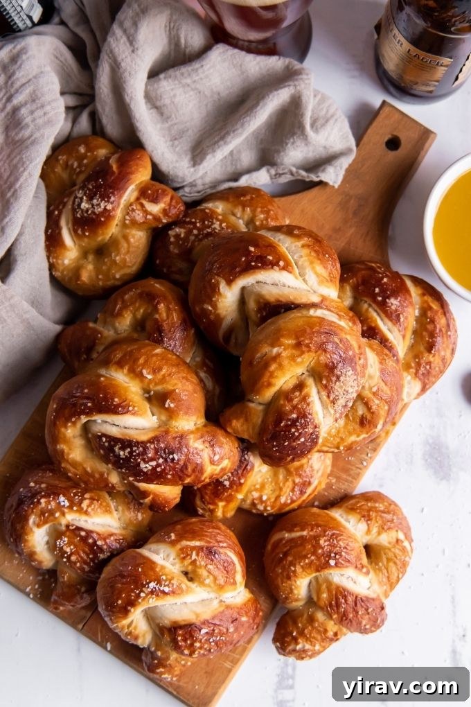 A generous pile of homemade soft pretzels arranged artfully on a wooden cutting board, accompanied by a small bowl of creamy maple mustard sauce, ready for dipping.