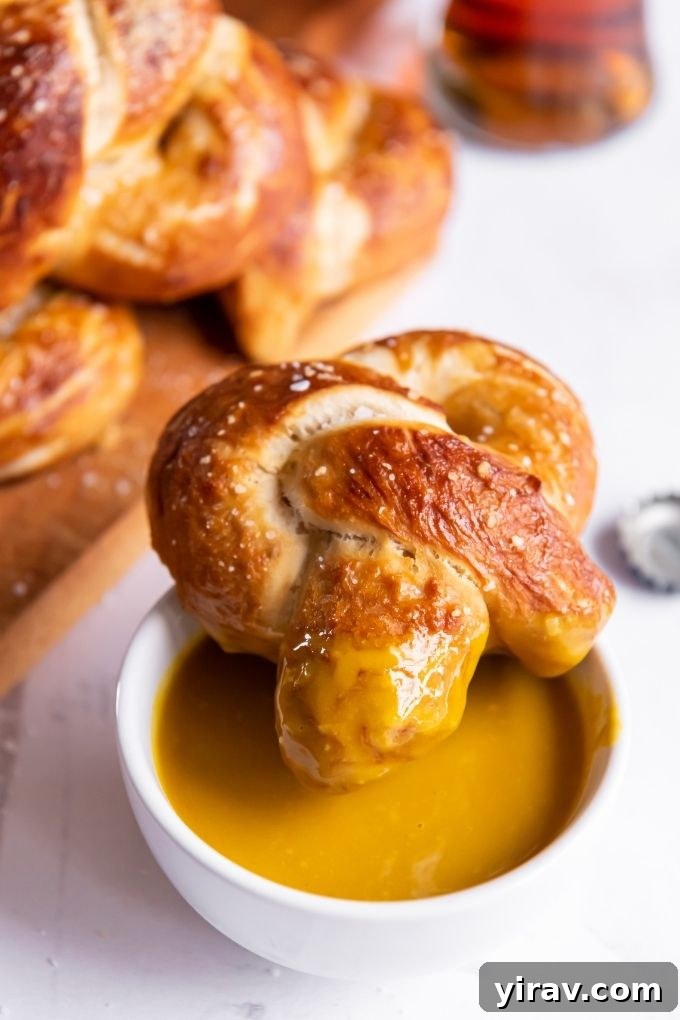 A single homemade soft pretzel, perfectly golden-brown and twisted, being dipped into a creamy maple mustard sauce, ready for a delicious bite.