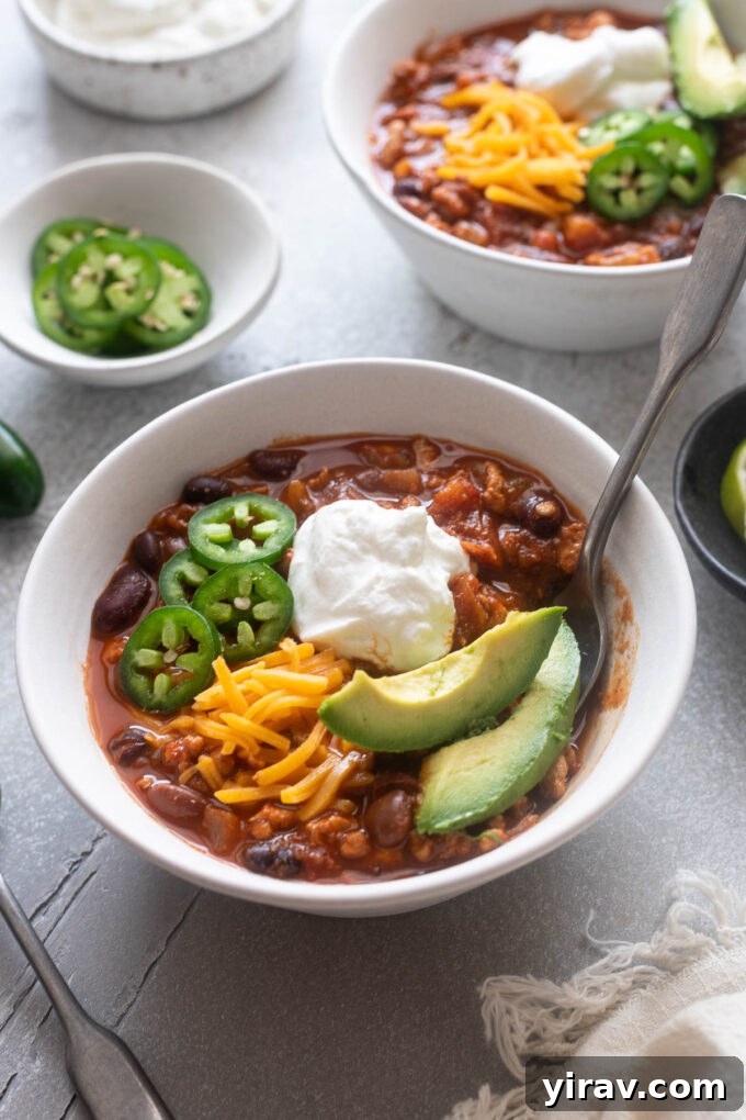 Bowl of ground chicken chili with a spoon digging in, garnished with fresh herbs and sour cream.