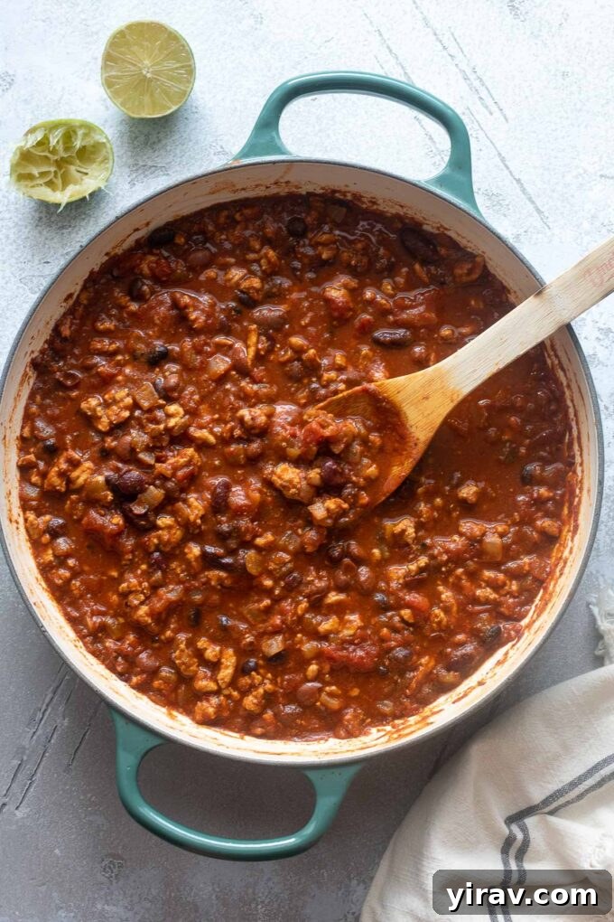 Ground chicken chili in a Dutch oven with a wooden spoon digging in.
