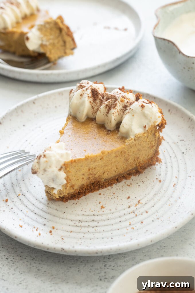 Autumn Spice Pumpkin Cheesecake Delight 7 Slice of pumpkin cheesecake pie on a plate with piped whipped cream.