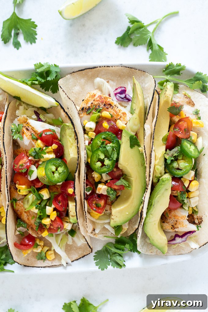 Close-up of a perfectly constructed cod fish taco, topped with the vibrant cherry tomato salsa, creamy avocado, and a slice of jalapeño.