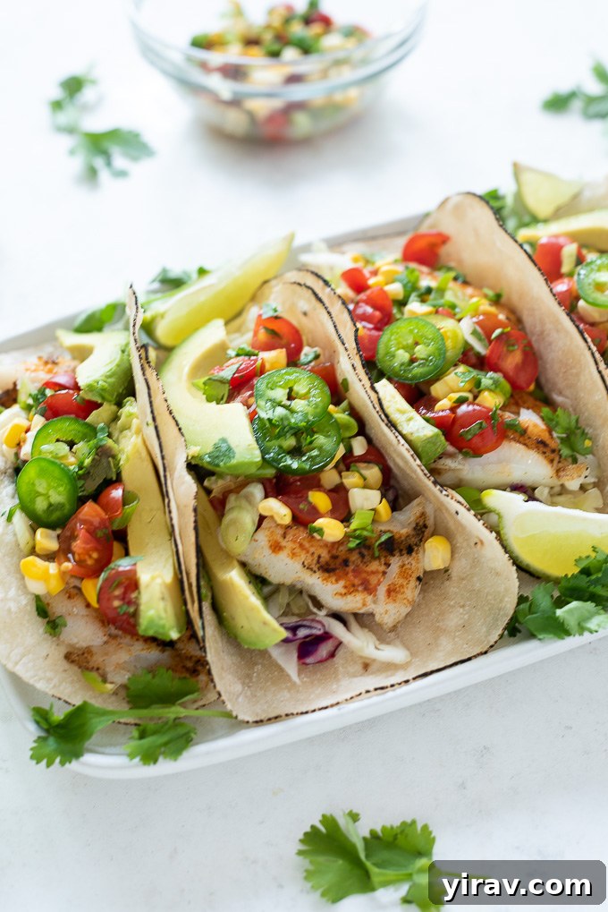Two grilled fish tacos on a white plate, garnished with fresh cilantro, a lime wedge, and a generous topping of cherry tomato salsa.